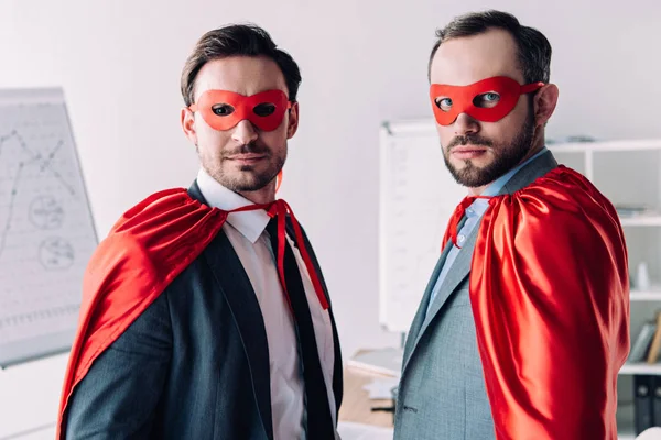 Retrato de guapos súper hombres de negocios en máscaras y capas en la oficina - foto de stock