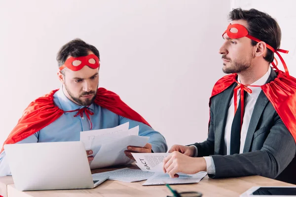 Beaux super hommes d'affaires en masques et capes travaillant avec des documents au bureau — Photo de stock