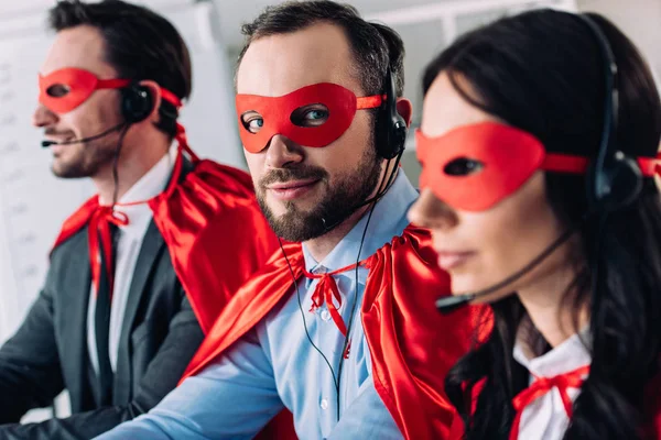 Super businesspeople in masks and headsets supporting customers in call center — Stock Photo