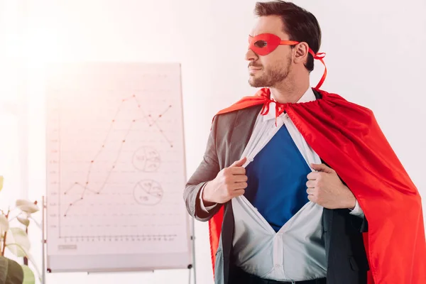 Handsome super businessman in mask and cape showing blue shirt in office — Stock Photo