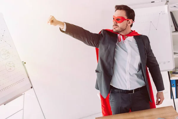 Beau super homme d'affaires en masque et cape debout avec la main au bureau — Photo de stock