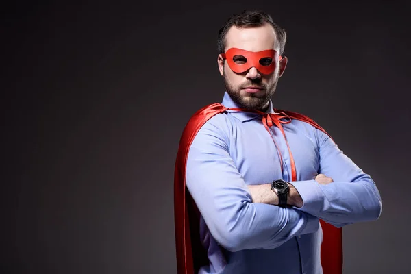 Handsome super businessman in mask and cape with crossed arms isolated on black — Stock Photo