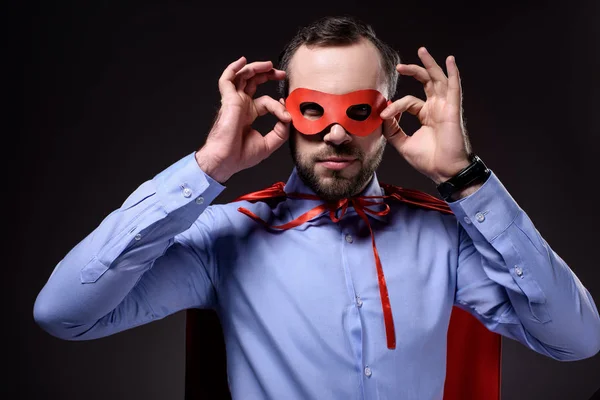 Handsome super businessman in cape holding mask isolated on black — Stock Photo