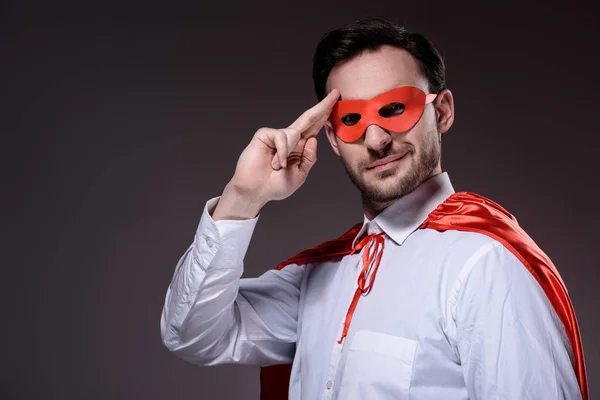 Schöner Superunternehmer in Maske und Umhang salutiert isoliert auf schwarz — Stockfoto