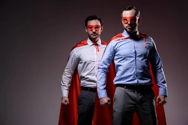 Красивые супер бизнесмены в масках и плащах, стоящие с кулаками, изолированными на сером — стоковое фото