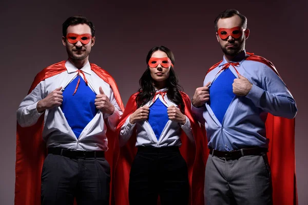 Super businesspeople in masks and capes showing blue shirts isolated on grey — Stock Photo