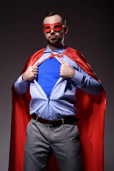 Guapo super hombre de negocios en máscara y capa mostrando camisa azul aislado en negro - foto de stock