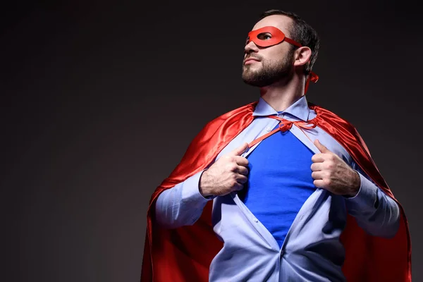 Bello super uomo d'affari in maschera e mantello che mostra camicia blu e guardando lontano isolato su nero — Foto stock