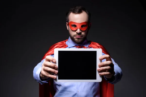 Beau super homme d'affaires en masque et cape montrant comprimé isolé sur noir — Photo de stock