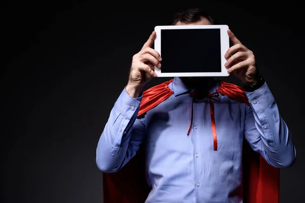 Super hombre de negocios en la capa que cubre la cara con la tableta aislada en negro — Stock Photo