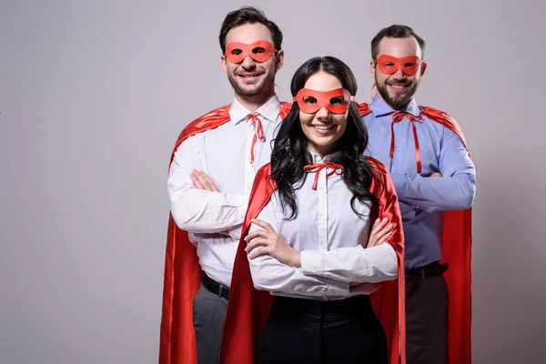 Super empresarios sonrientes con máscaras y capas con brazos cruzados aislados en gris - foto de stock