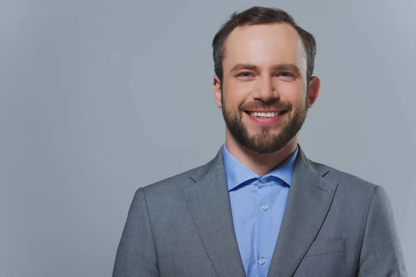 Smiling handsome businessman looking at camera isolated on grey — Stock Photo