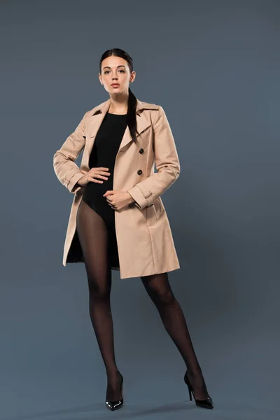 Slim woman in black pantyhose and beige trench on dark background — Stock Photo