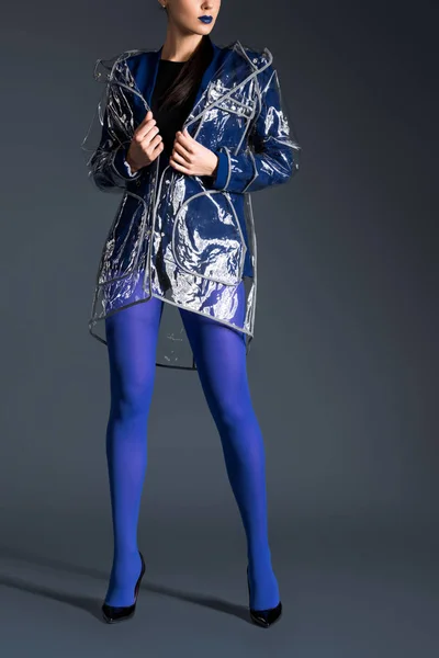 Femme élégante en collants bleus et imperméable transparent sur fond sombre — Photo de stock