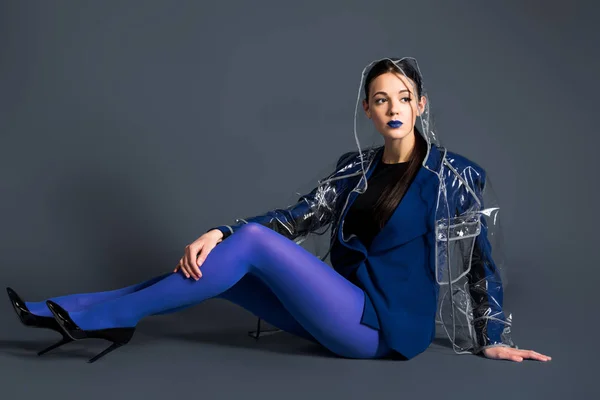 Femme mince en collants bleus et imperméable couché sur fond sombre — Photo de stock