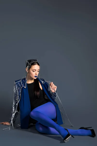 Chica en ropa azul y impermeable transparente acostado sobre fondo oscuro - foto de stock