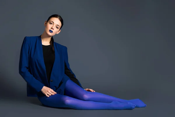 Fashionable woman in blue pantyhose and jacket lying on dark background — Stock Photo