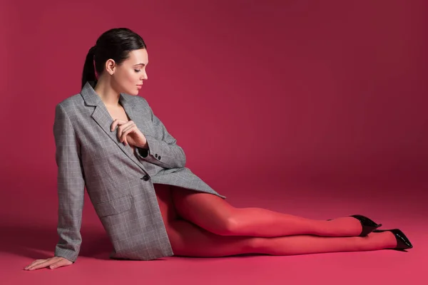 Mujer delgada en pantimedias rojas y chaqueta gris acostada sobre fondo rojo - foto de stock