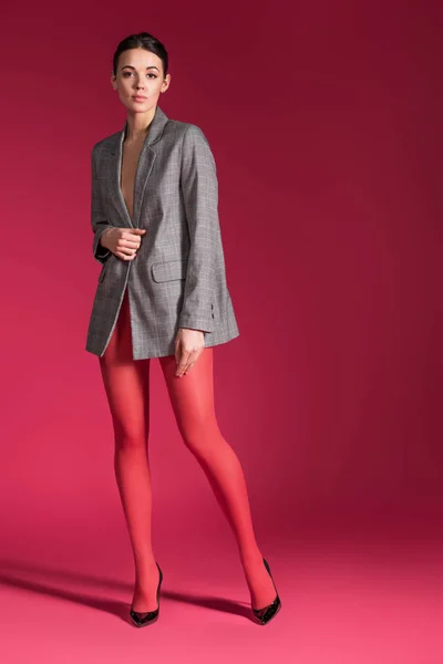 Mujer sensual en medias de nylon rojo con chaqueta gris sobre fondo rojo - foto de stock