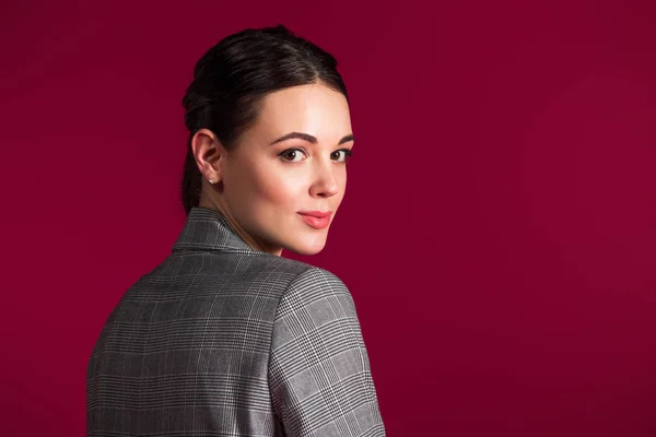 Chica sonriente en chaqueta gris posando aislada sobre fondo rojo - foto de stock