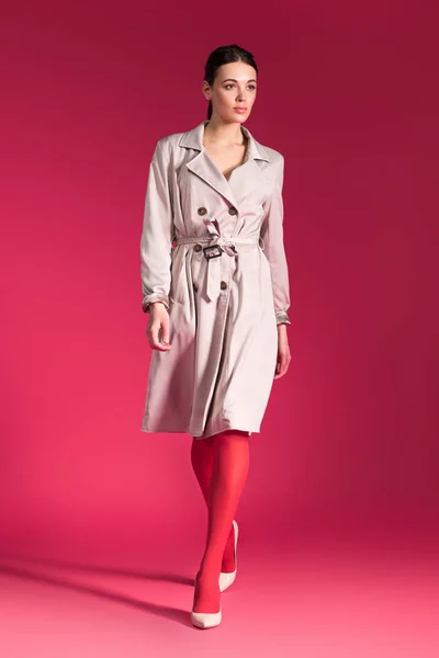 Woman walking in beige trench and heel shoes on red background — Stock Photo