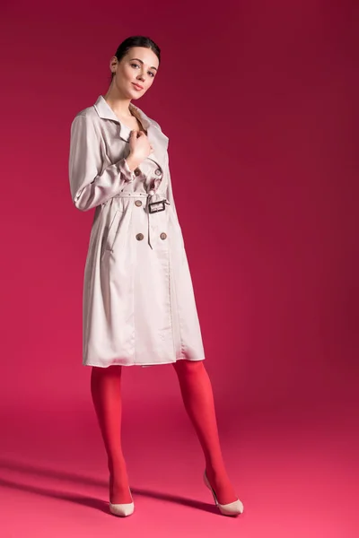 Smiling girl wearing beige trench and high heels on red background — Stock Photo