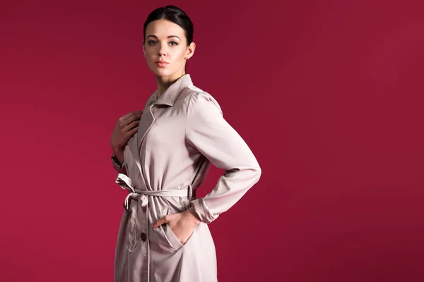 Mulher atraente em trincheira bege posando isolado no fundo vermelho — Fotografia de Stock