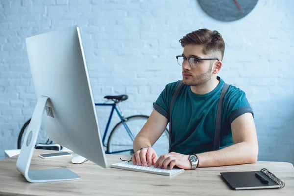 Schöner junger Mann mit Brille arbeitet mit Desktop-Computer — Stockfoto