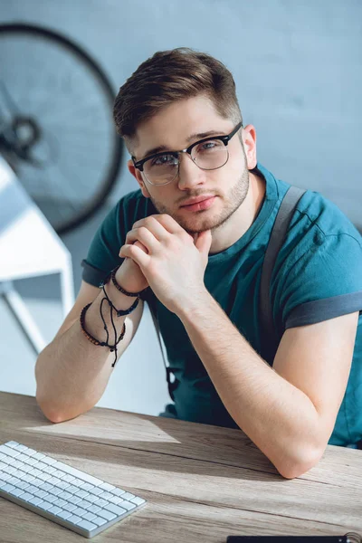 Jovem bonito em óculos olhando para a câmera enquanto trabalhava em casa — Fotografia de Stock