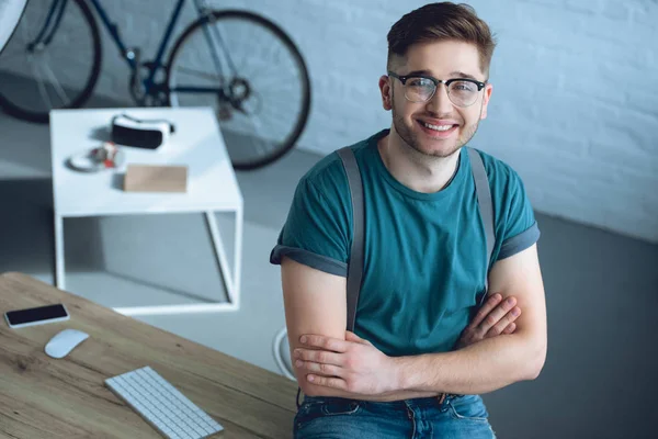 Handsome young man in eyeglasses standing with crossed arms and smiling at camera — Stock Photo