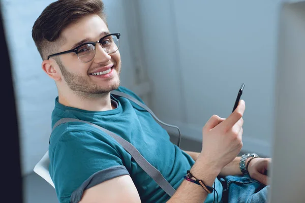 Cheerful young man using smartphone and smiling at camera — Stock Photo