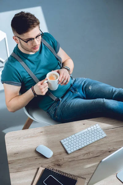 High angle view of young freelancer drinking coffee and working at home office — Stock Photo