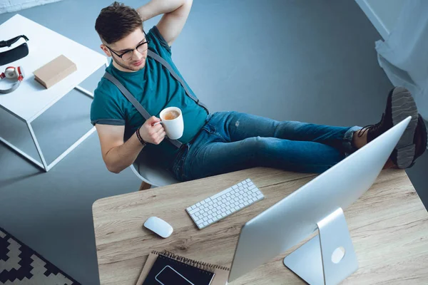 Vista ad alto angolo del giovane che beve caffè e lavora a casa ufficio — Foto stock