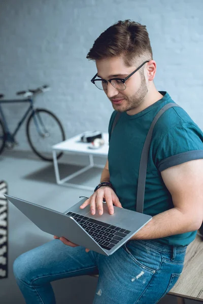 Handsome young freelancer in eyeglasses using laptop at home — Stock Photo