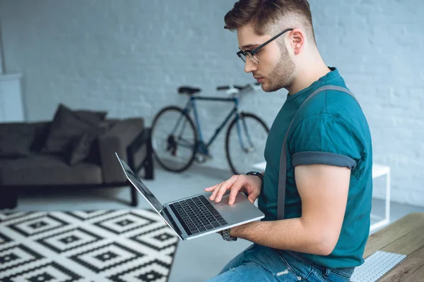 Side view of handsome young freelancer in eyeglasses using laptop — Stock Photo