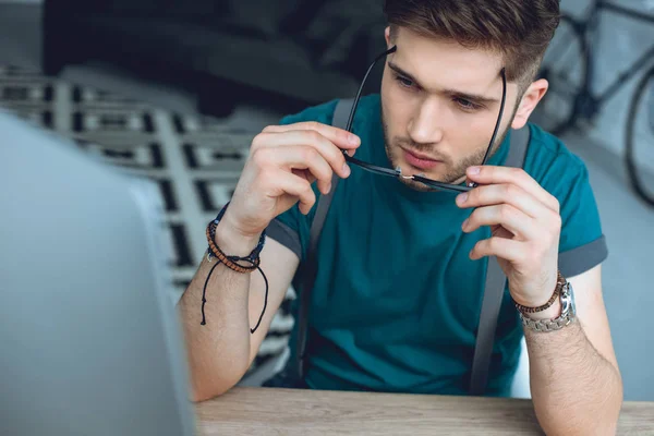 Focused young man wearing eyeglasses and using desktop computer at home office — Stock Photo