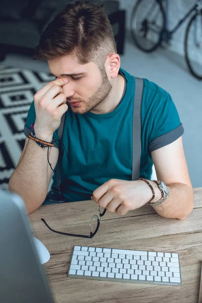 Stanco giovane uomo che tiene gli occhiali e sfregamento naso mentre lavora a casa ufficio — Foto stock