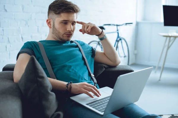 Jovem focado usando laptop enquanto sentado no sofá — Fotografia de Stock