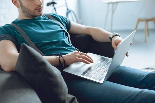 Tiro cortado de jovem usando laptop enquanto sentado no sofá — Fotografia de Stock