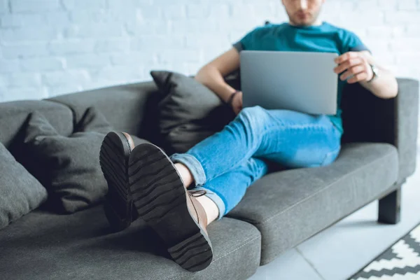 Tiro cortado de jovem usando laptop no sofá em casa — Fotografia de Stock