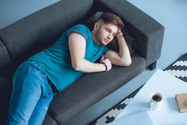 High angle view of handsome young man lying on couch and looking away at home — Stock Photo