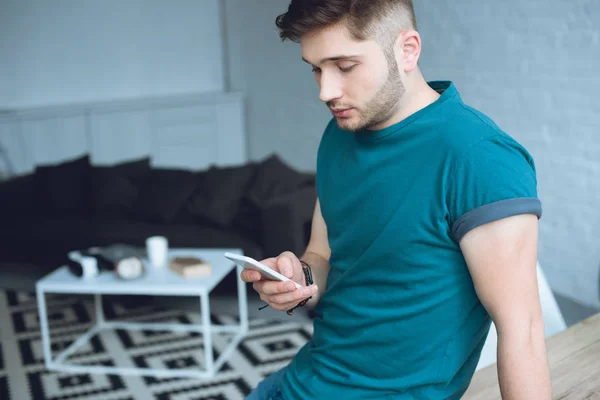 Bello giovane uomo utilizzando smartphone a casa — Foto stock