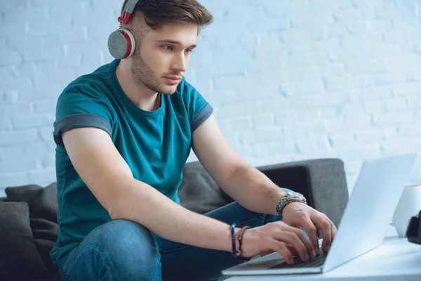 Hombre joven enfocado en los auriculares usando el ordenador portátil en casa - foto de stock