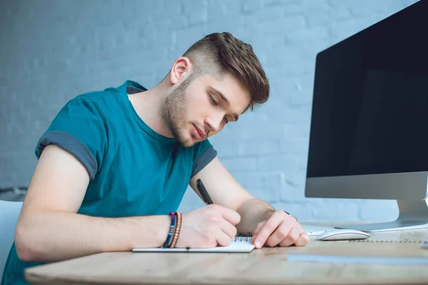 Focused young man writing in notebook while working at home office — Stock Photo