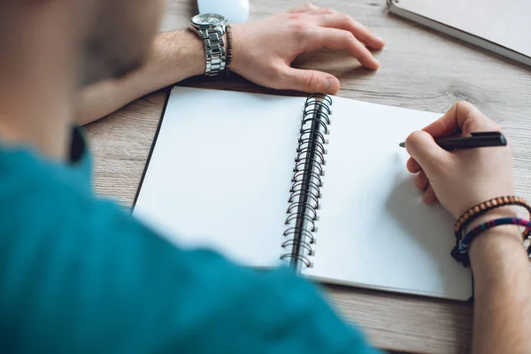 Selective focus of young man taking notes in blank notebook — Stock Photo