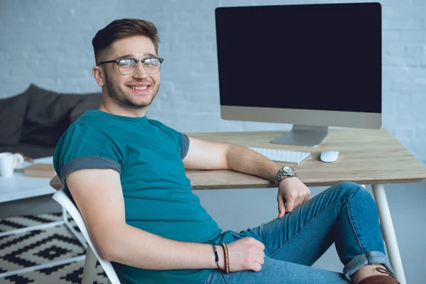 Joven barbudo sentado junto a la mesa de trabajo con ordenador - foto de stock