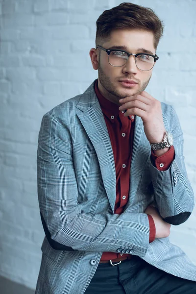 Atractivo hombre barbudo con traje y gafas delante de la pared blanca - foto de stock