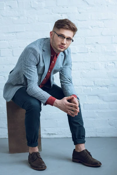 Stylish man in casual clothes sitting in front of brick wall — Stock Photo