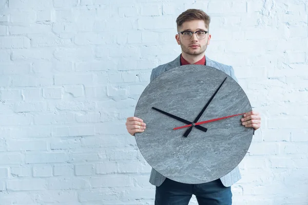 Man holding large clock in front of him by white wall — Stock Photo