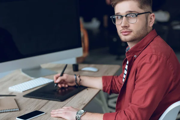 Бородач сидит за столом с компьютером и графическим планшетом — стоковое фото